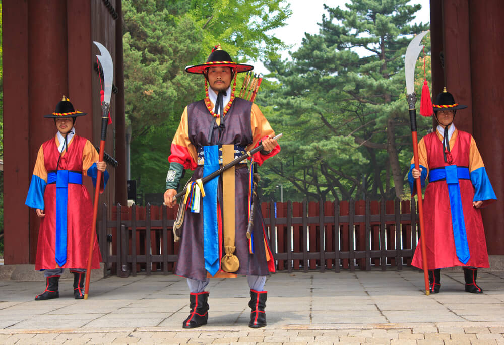 Palace guards in traditional costumes solemnly guard the imposing main gate of Deoksugung Palace in downtown Seoul, South Korea.