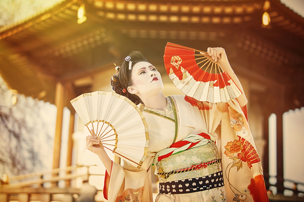 beautiful japanese woman dressed as geisha dancing with fans against Peace Pagoda in Battersea Park in London